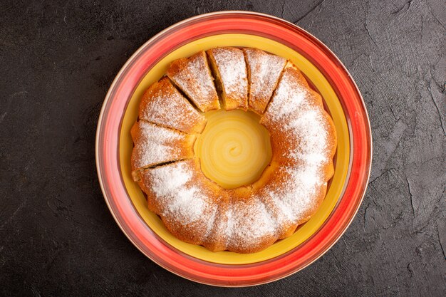 Una vista superior dulce pastel redondo con polvo de azúcar en rodajas dulce delicioso pastel aislado dentro de la placa y fondo gris galleta galleta de azúcar