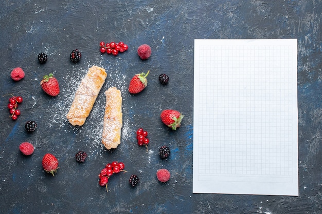 Vista superior dulces deliciosos brazaletes con relleno delicioso horneado con frutas y bayas papel en blanco sobre el escritorio oscuro hornear pastel galleta azúcar postre dulce