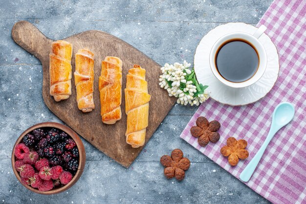 Vista superior dulces deliciosos brazaletes con relleno junto con una taza de café, galletas, bayas en el escritorio gris, azúcar dulce, hornear, pastelería, galleta, galleta