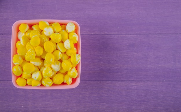 Vista superior de dulces dulces amarillos en un recipiente sobre fondo de madera púrpura con espacio de copia