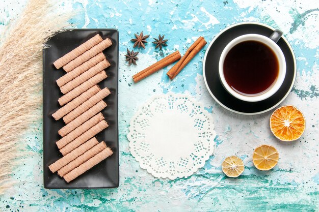 Vista superior dulces galletas largas con taza de té y canela sobre fondo azul.