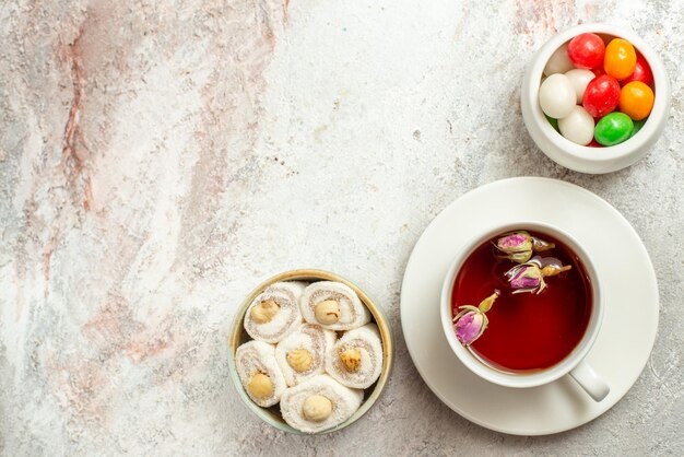 Vista superior de dulces con una taza de té, cuencos de dulces delicias turcas y una taza de té sobre el fondo blanco.