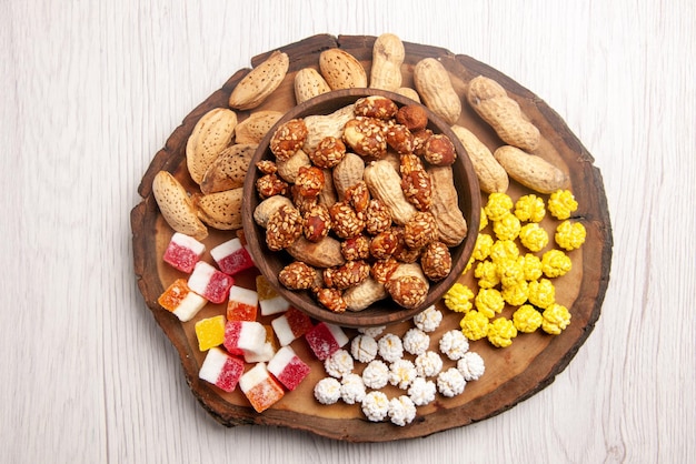 Vista superior de los dulces en un tazón de cacahuetes en un tazón junto a los caramelos de colores en la tabla de madera