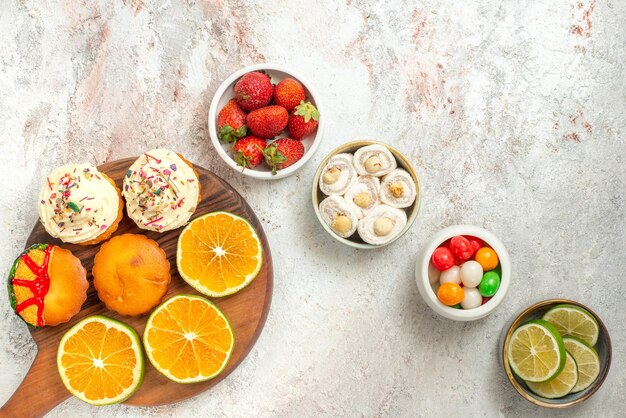 Vista superior de los dulces en tazones cuatro tazones de dulces delicias turcas y rodajas de limón y la tabla de cortar de madera con galletas y naranja sobre la mesa