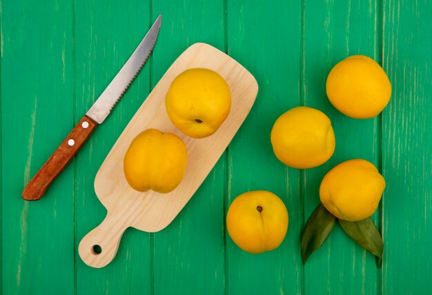 Vista superior de duraznos amarillos frescos en una tabla de cocina de madera con cuchillo sobre un fondo de madera verde