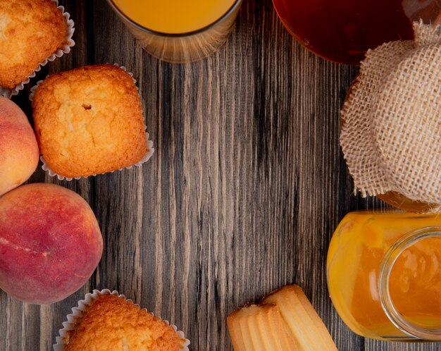 Vista superior de duraznos frescos con magdalenas galletas vaso de jugo de durazno y mermelada de durazno en un frasco de vidrio en madera rústica con espacio de copia