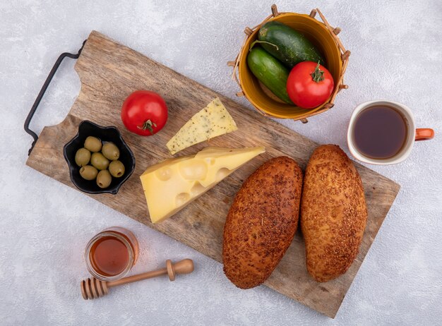 Vista superior de empanadas de sésamo en una tabla de cocina de madera con aceitunas verdes en un tazón negro con queso y un tazón de pepinos y tomates sobre un fondo blanco.