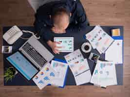 Foto gratuita vista superior del empresario con tablet pc analizando gráficos y documentos financieros, sentado en el escritorio en la oficina corporativa