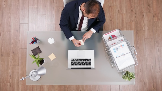 Vista superior del empresario en traje hablando por teléfono mientras escribe ideas en notas stickey trabajando en estrategia financiera después de analizar documentos de la empresa. reunión de inversiones de planificación de hombre emprendedor