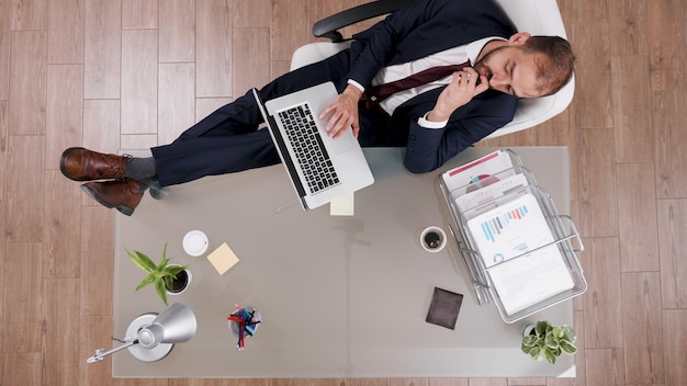 Vista superior del empresario en traje manteniendo los pies sobre el escritorio mientras escribe las estadísticas de la empresa