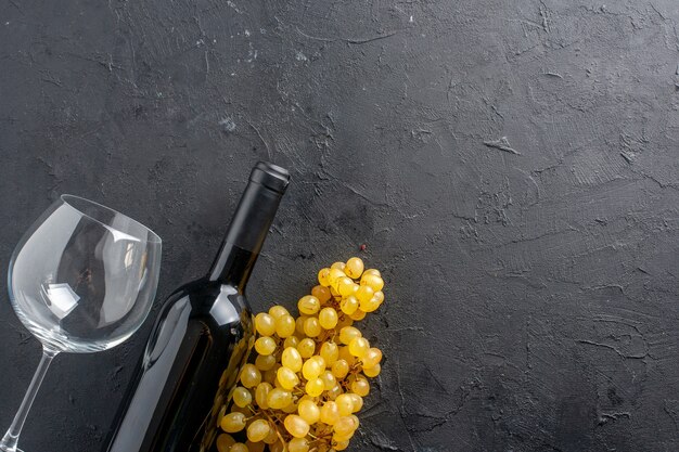 Vista superior encantadora botella de vino de uvas amarillas y abridor de vino de vidrio en una mesa oscura con espacio de copia