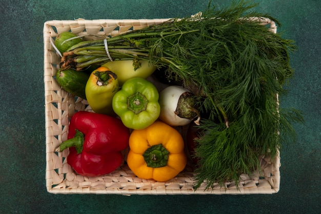 Vista superior de eneldo con pimiento y pepinos en una canasta sobre un fondo verde