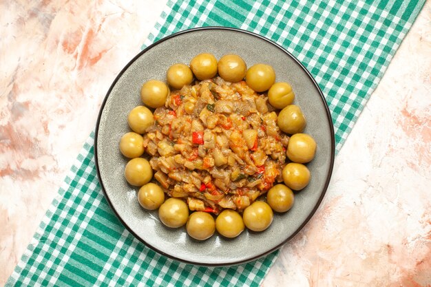 Vista superior de ensalada de berenjena asada y ciruelas en escabeche en placa sobre superficie a cuadros blanco turquesa