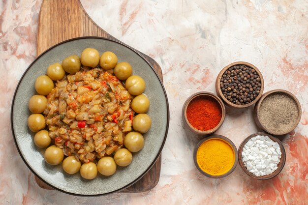 Vista superior de ensalada de berenjena asada y ciruelas en escabeche en un plato sobre una tabla de cortar sobre una superficie desnuda