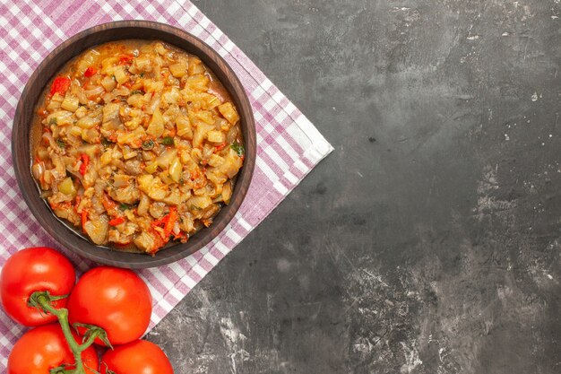 Vista superior de ensalada de berenjena asada en tomates de tazón sobre superficie a cuadros rosa blanca