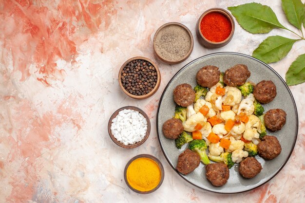 Vista superior de ensalada de brócoli y coliflor y albóndigas en un plato de diferentes especias en tazones pequeños sobre fondo aislado desnudo lugar libre