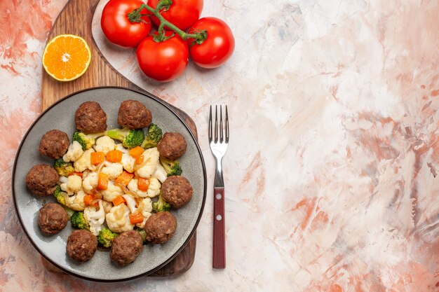 Foto gratuita vista superior de ensalada de brócoli y coliflor y albóndigas en un plato y una rodaja de limón en una tabla de cortar un tenedor de tomates en el espacio libre de fondo aislado desnudo