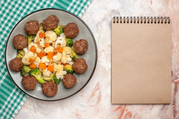 Foto gratuita vista superior de ensalada de brócoli y coliflor y albóndigas en un plato servilleta a cuadros verde y blanco un cuaderno sobre fondo aislado desnudo