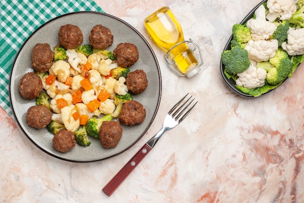 Vista superior ensalada de brócoli y coliflor y albóndigas en un plato servilleta a cuadros verde y blanco un tenedor aceite verduras crudas en un plato sobre fondo aislado desnudo