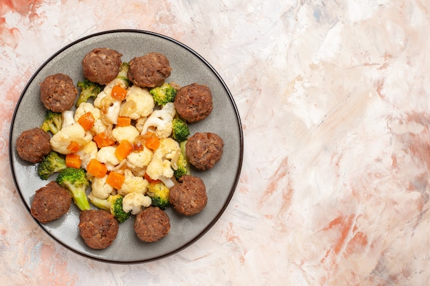 Vista superior de ensalada de brócoli y coliflor y albóndigas en un plato sobre una superficie aislada desnuda con espacio de copia