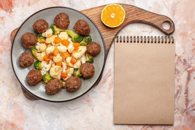 Foto gratuita vista superior de ensalada de brócoli y coliflor y rodaja de albóndiga y limón en un plato sobre una tabla de cortar un cuaderno sobre fondo aislado desnudo