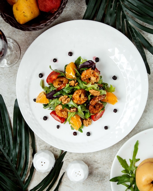 Vista superior de ensalada de camarones fritos con lechuga, rúcula, naranja y tomate