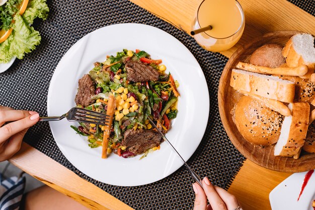 Vista superior ensalada de carne de res a la parrilla con tomate lechuga pepino de maíz y palito de pan en un plato