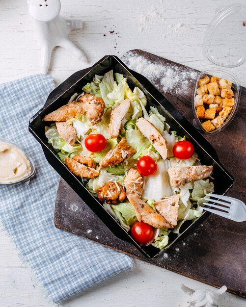 Vista superior de ensalada César con pollo y tomates cherry en una tabla para cortar madera