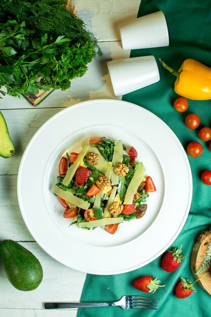 Vista superior de ensalada fresca con nueces de queso parmesano, tomates cherry y fresas en un tazón blanco