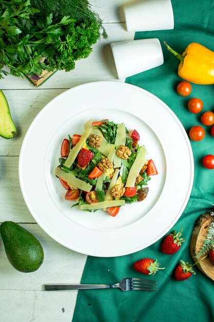 Vista superior de ensalada fresca con nueces de queso parmesano, tomates cherry y fresas en un tazón blanco