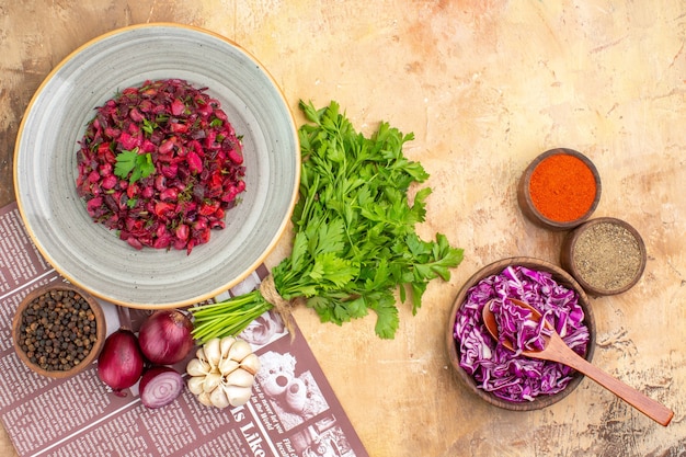 Vista superior de ensalada fresca en un plato de cerámica con cebollas rojas, ajo, perejil, pimienta negra molida, cúrcuma y col roja en un cuenco de madera sobre un fondo claro con lugar para copiar