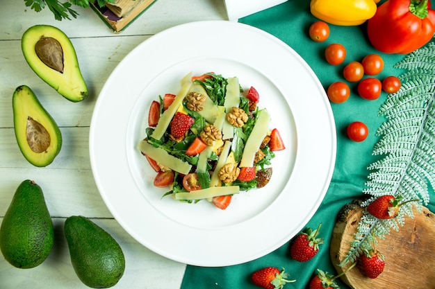 Vista superior de ensalada fresca con queso parmesano, aguacate, nueces, tomates cherry y fresas en un tazón blanco