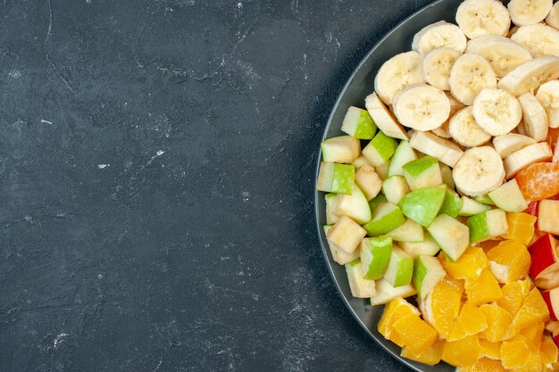 Vista superior ensalada de frutas frescas en rodajas plátanos manzanas y naranjas sobre fondo oscuro