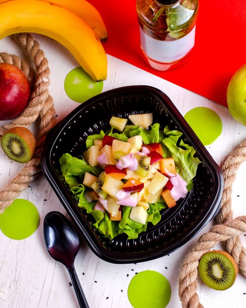 Vista superior de ensalada de frutas con kiwi y plátanos en una caja de entrega