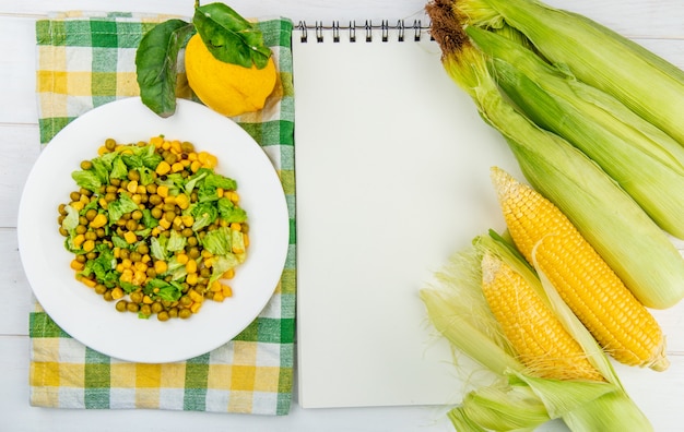 Vista superior de ensalada de maíz sobre tela y limón con mazorcas de maíz y notas sobre superficie de madera