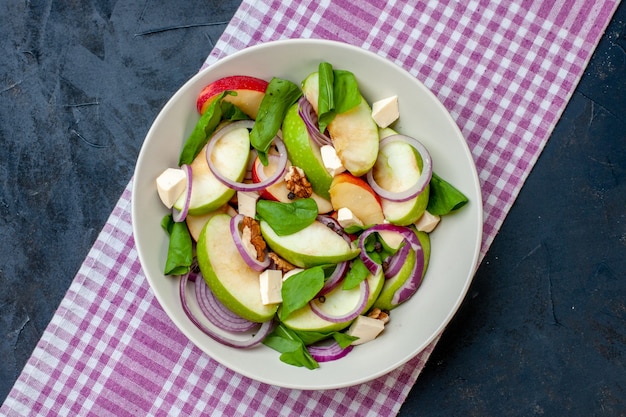 Foto gratuita vista superior ensalada de manzana fresca en plato blanco mantel a cuadros blanco púrpura sobre mesa azul oscuro