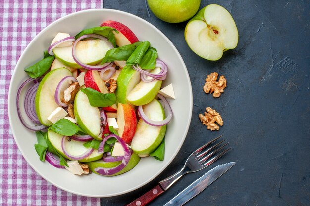 Foto gratuita vista superior ensalada de manzana fresca en plato redondo manzanas verdes nuez mantel a cuadros morado y blanco tenedor y cuchillo sobre mesa oscura