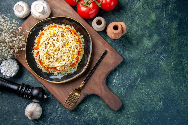 Vista superior de la ensalada de mimosa dentro de la placa con champiñones y tomates sobre el fondo azul oscuro