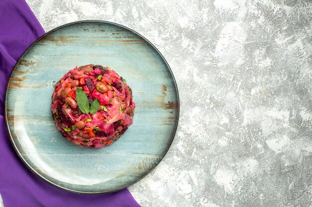 Vista superior de ensalada de papa con vinagreta y remolacha en plato redondo chal morado en mesa de luz con espacio libre