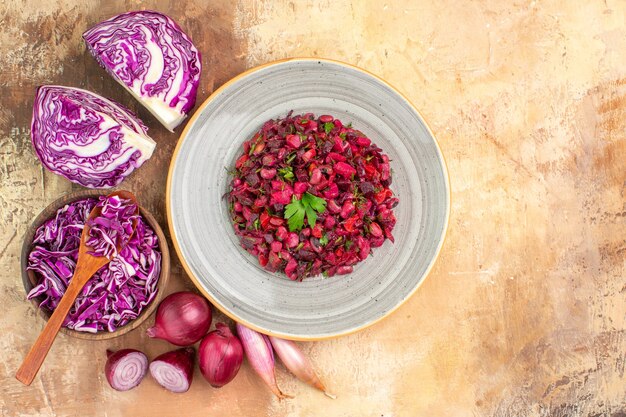 Vista superior ensalada de remolacha fresca aderezada con perejil en un plato hecho de cebollas rojas, repollo y otras verduras sobre un fondo de madera con espacio de copia a la derecha