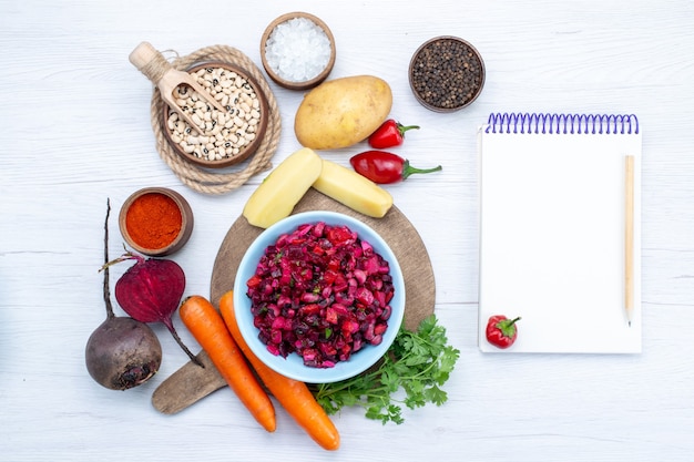 Vista superior de ensalada de remolacha fresca con verduras en rodajas junto con frijoles crudos, zanahorias, patatas, bloc de notas en el escritorio de luz, comida comida ensalada fresca