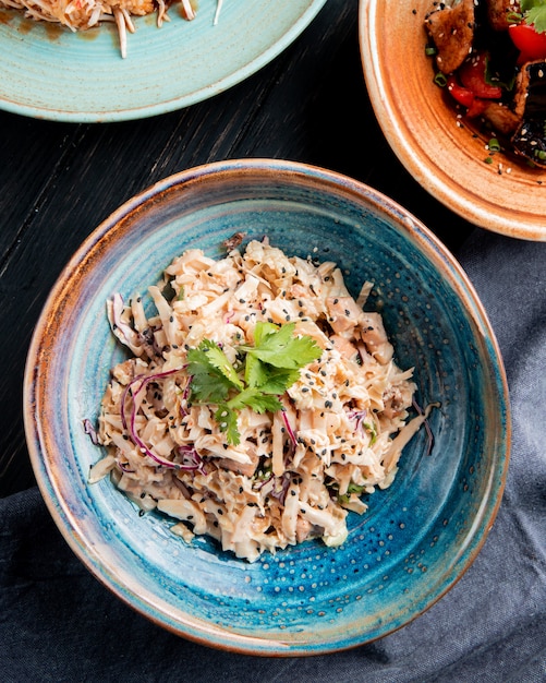 Vista superior de ensalada con repollo picado pollo y semillas negras en un plato sobre superficie de madera