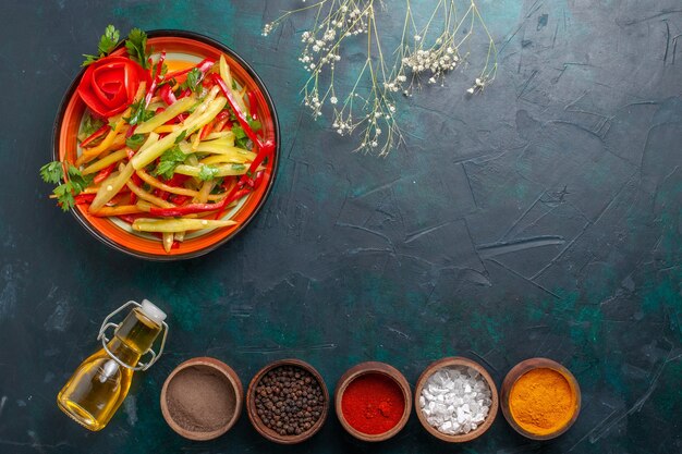 Vista superior ensalada saludable de pimientos en rodajas con aceite de oliva y condimentos sobre fondo azul oscuro