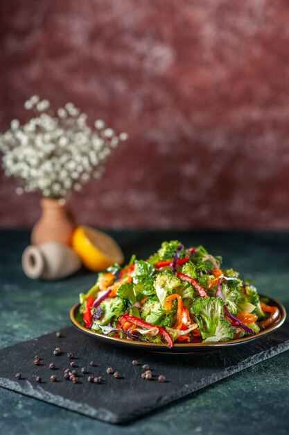 Vista superior de ensalada vegana con ingredientes frescos en un plato y pimienta sobre tabla de cortar negra