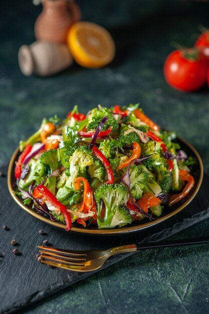 Vista superior de ensalada vegana con ingredientes frescos en un plato y pimienta sobre tabla de cortar negra
