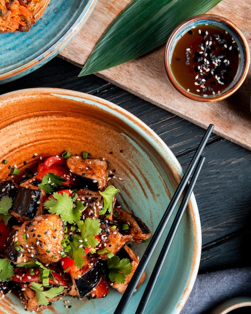 Foto gratuita vista superior de ensalada de verduras con berenjenas fritas tomates hierbas y sésamo en un tazón servido con salsa de soja sobre madera