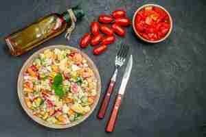 Foto gratuita vista superior de ensalada de verduras con botella de aceite de tomate y cubiertos en el lado sobre fondo gris oscuro