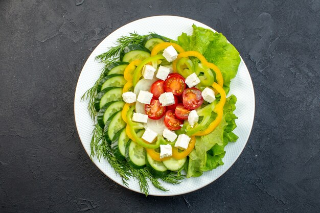 Vista superior ensalada de verduras se compone de rodajas de pepinos, tomates, pimienta y queso sobre fondo oscuro