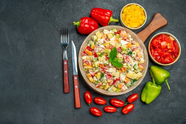 Vista superior de ensalada de verduras con cubiertos y verduras en el lateral con lugar libre para el texto sobre fondo gris oscuro