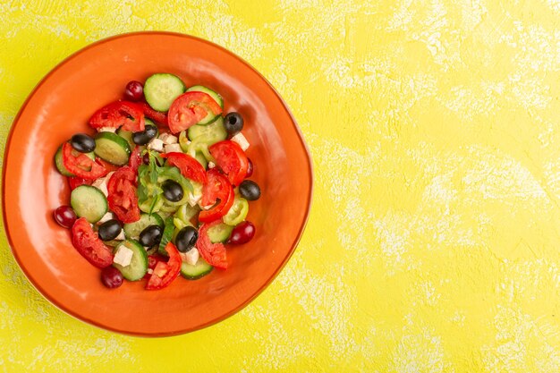 Vista superior Ensalada de verduras frescas con pepinos en rodajas, tomates, aceituna, placa interior sobre el fondo amarillo, comida vegetal, ensalada, comida, fotografía en color